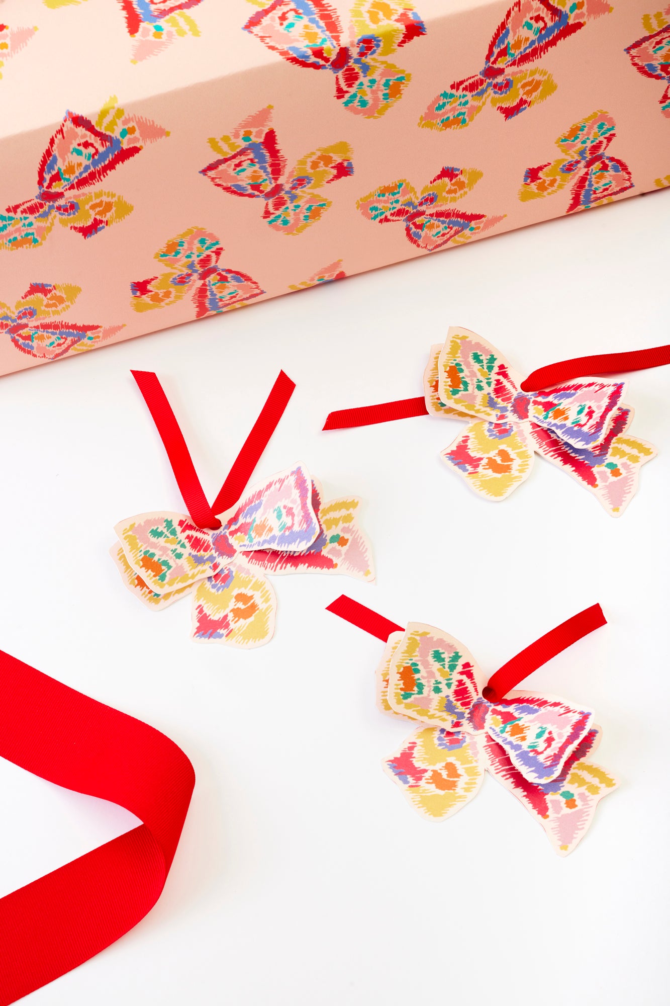 Colorful patterned bows with red ribbons placed next to matching gift wrap.