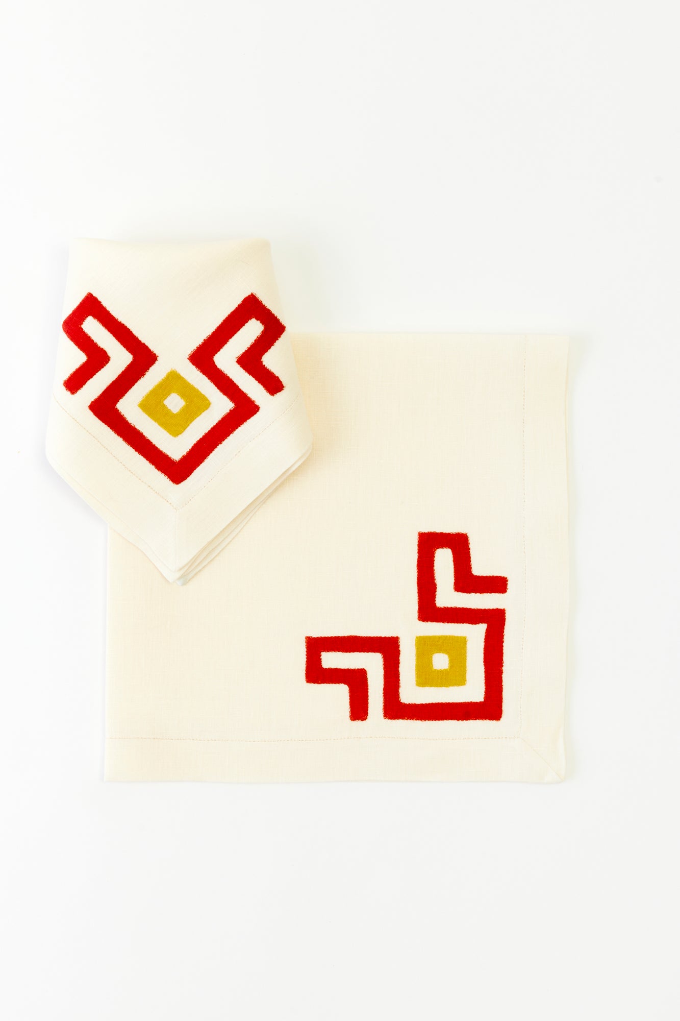 Cream linen napkin and placemat set with bold red and yellow geometric embroidery, perfect for modern table settings.