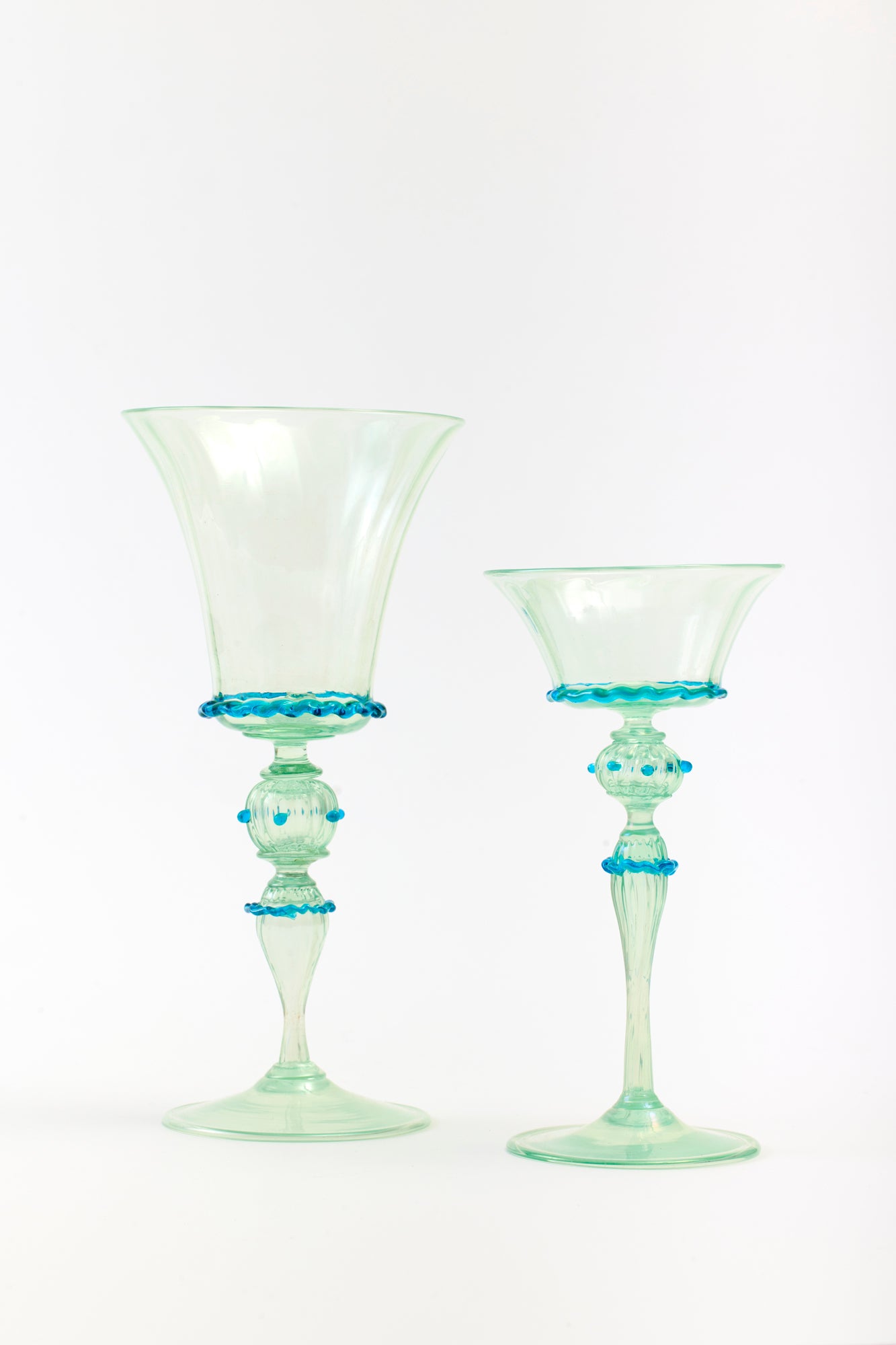 Close-up of elegant vintage Venetian green glass goblet and coupe with blue decorative accents on the stems.