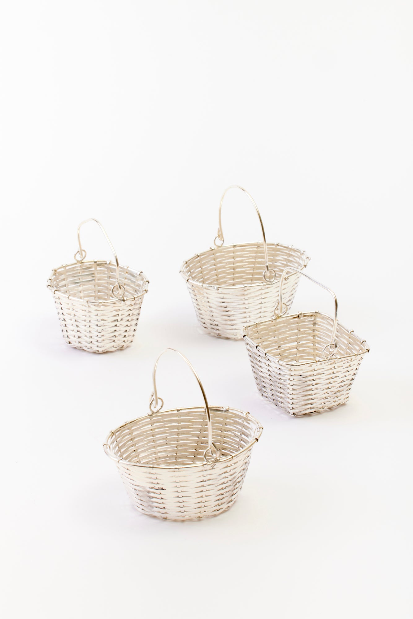 Photograph of 4 silver baskets against a white background. Each basket varies in size and shape and are made of woven silver. 