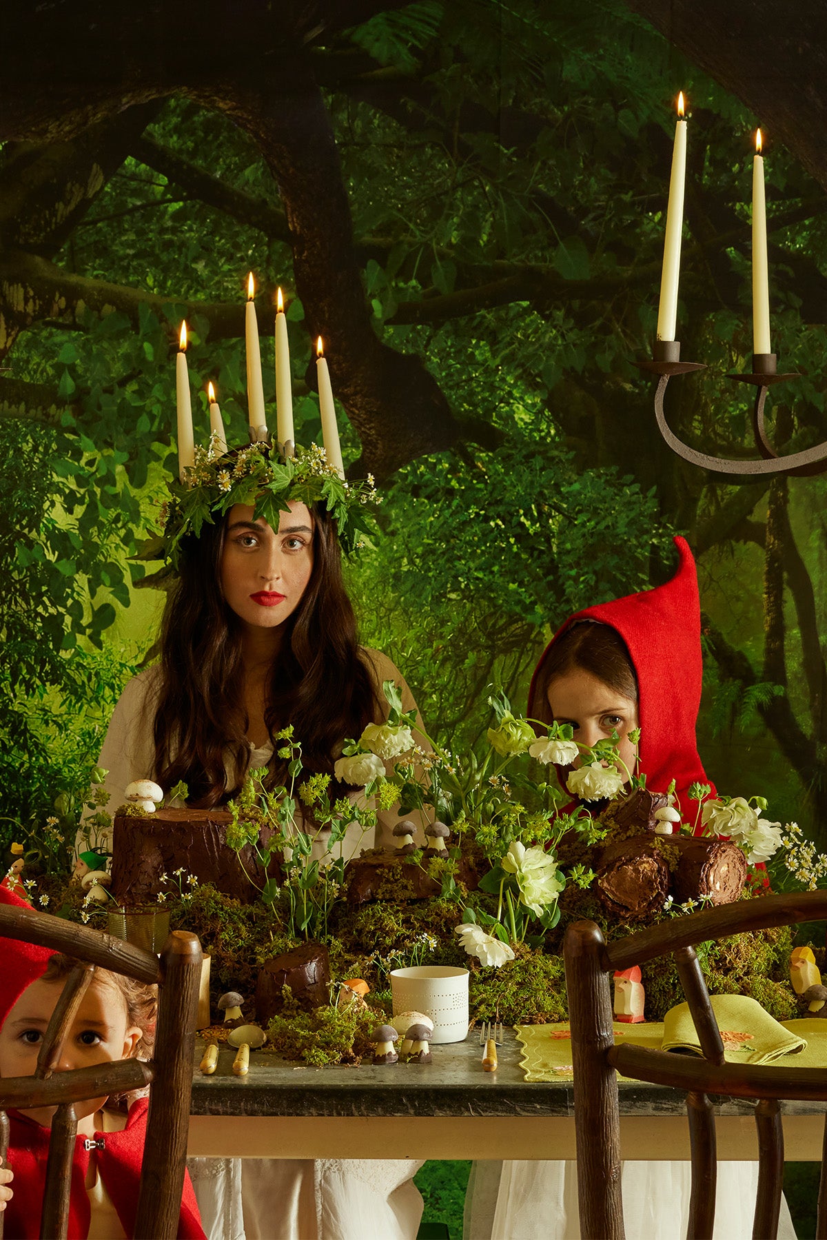 A captivating, ethereal tablescape set in a lush, forest-like atmosphere, where a woman in a white dress wears a crown of ivy and candles. Surrounded by moss, mushrooms, and tiny woodland figurines, the scene evokes a mystical forest feast, with a lime green placemat adding a playful touch to the rustic charm.