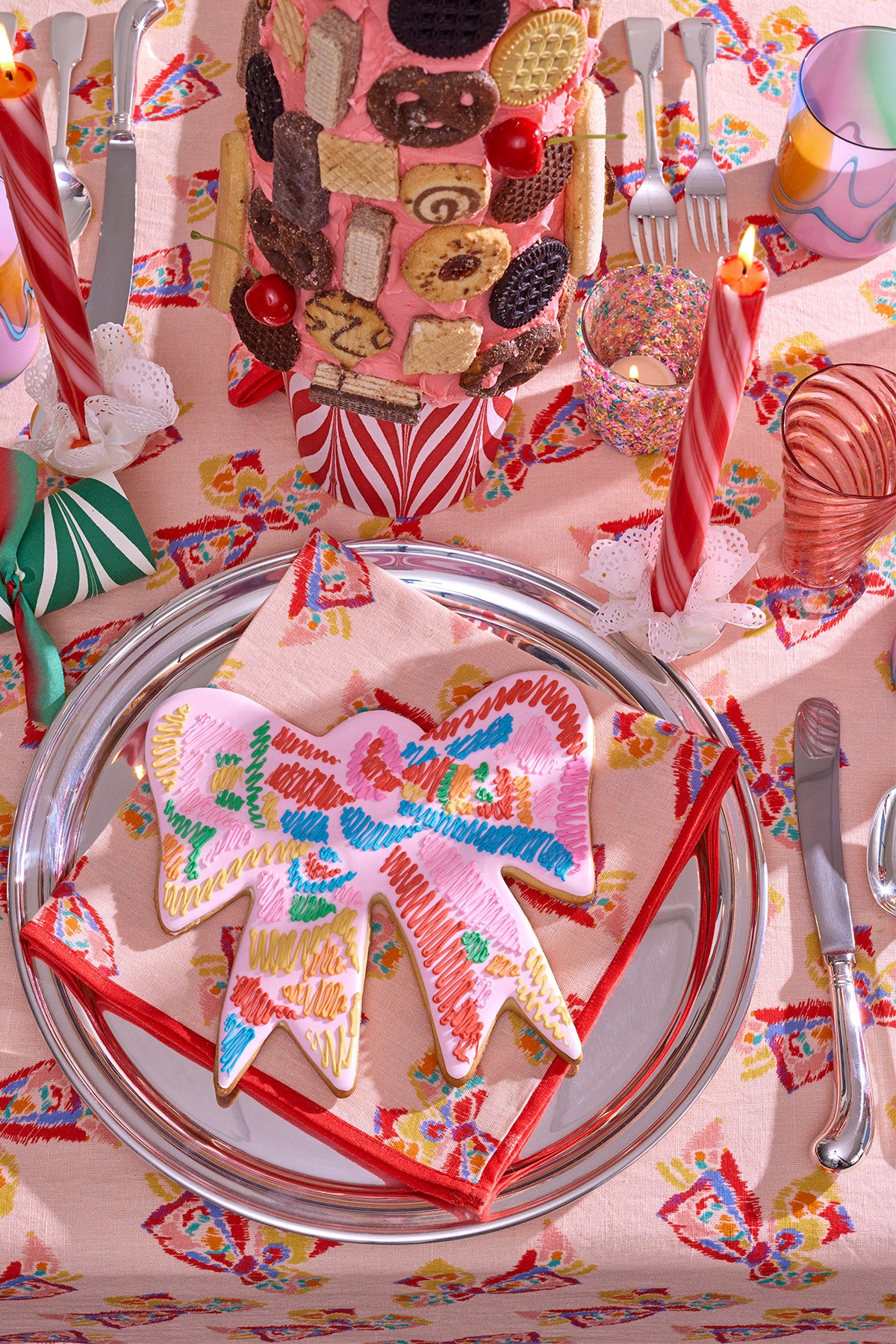 Photograph of a Christmas inspired table setting, featuring peppemint twist taper candles, marbled paper party crackers, silver platters, hand blown glass goblets, printed linen napkins and tablecloth, and an arrangement of desserts. 