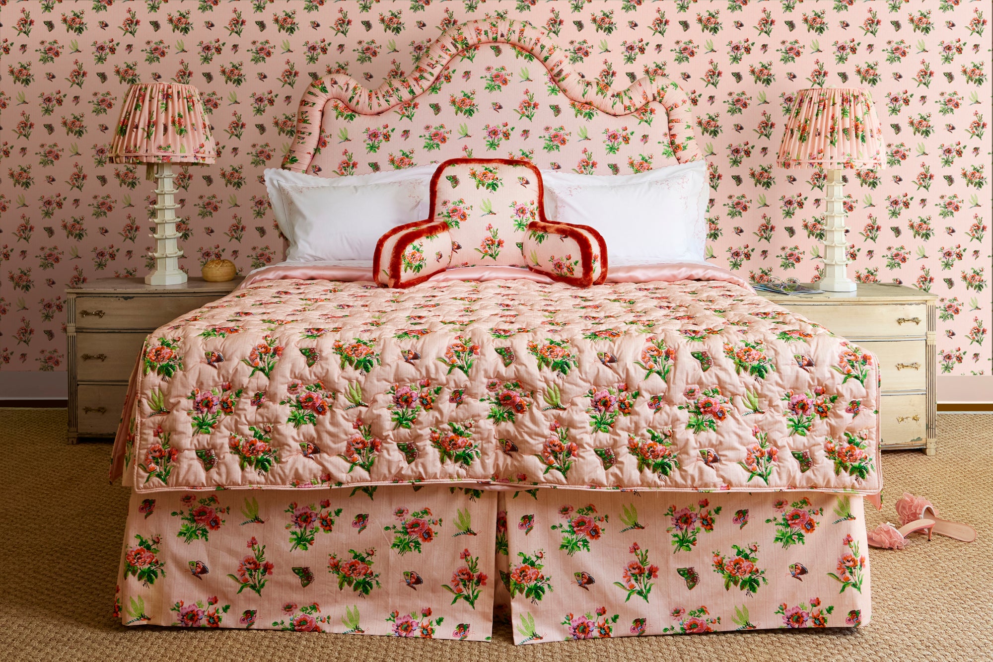 Bedroom with pink chintz bedding and wallpaper, featuring coordinating lampshades and a bed with a matching headboard.