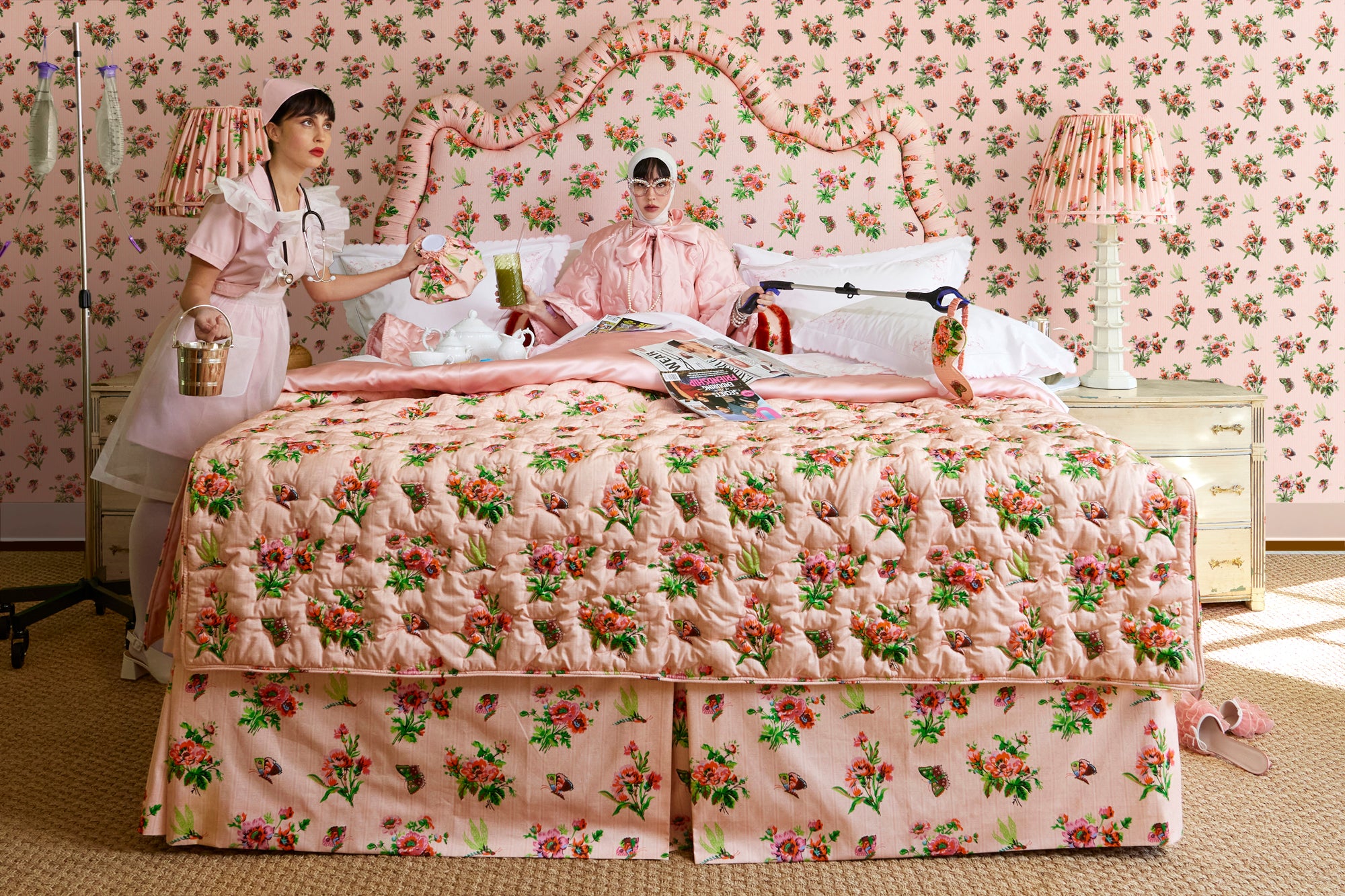 Nurse and patient in bedroom with pink chintz bedding and wallpaper, featuring coordinating lampshades and a bed with a matching headboard.