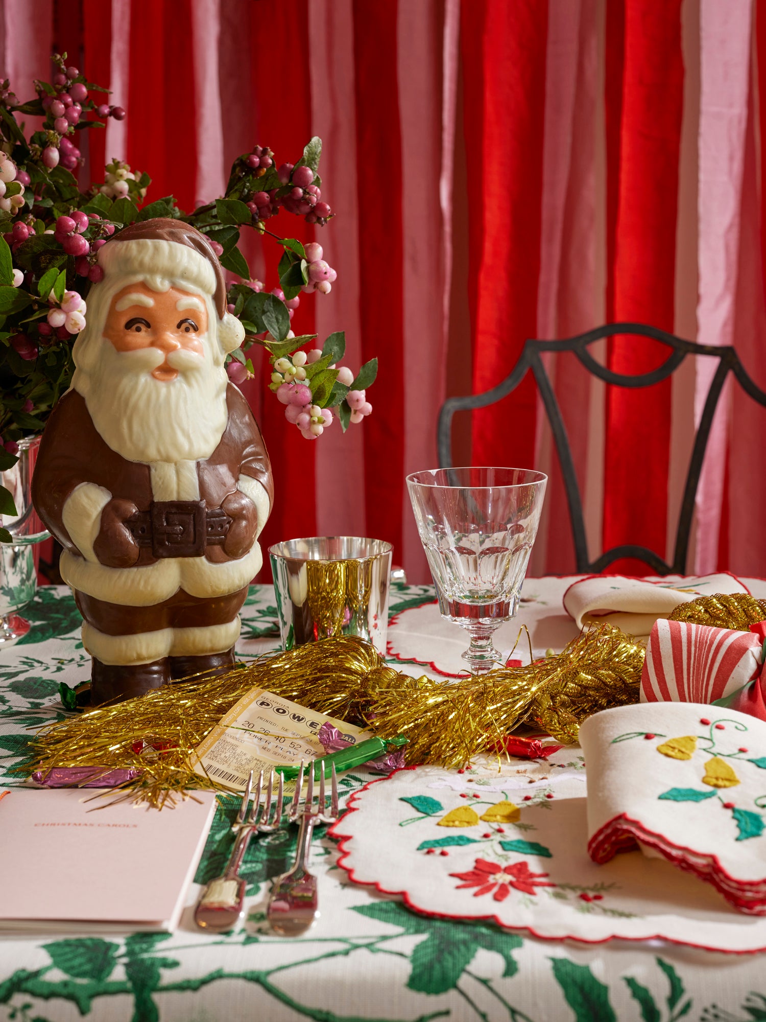 Christmas themed table setting featuring silver tumbler, crystal goblet, linen placemat and napkin with French embroidered appliqué, fresh florals, and a chocolate Santa. 