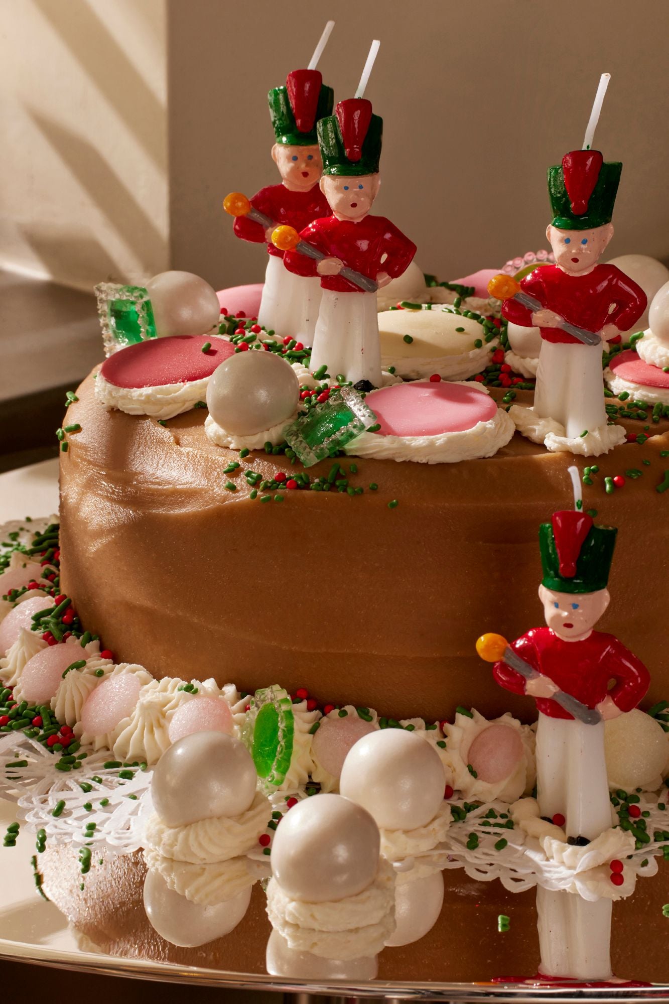 Decorative cake with Christmas-themed figures and icing decorations on a reflective surface.