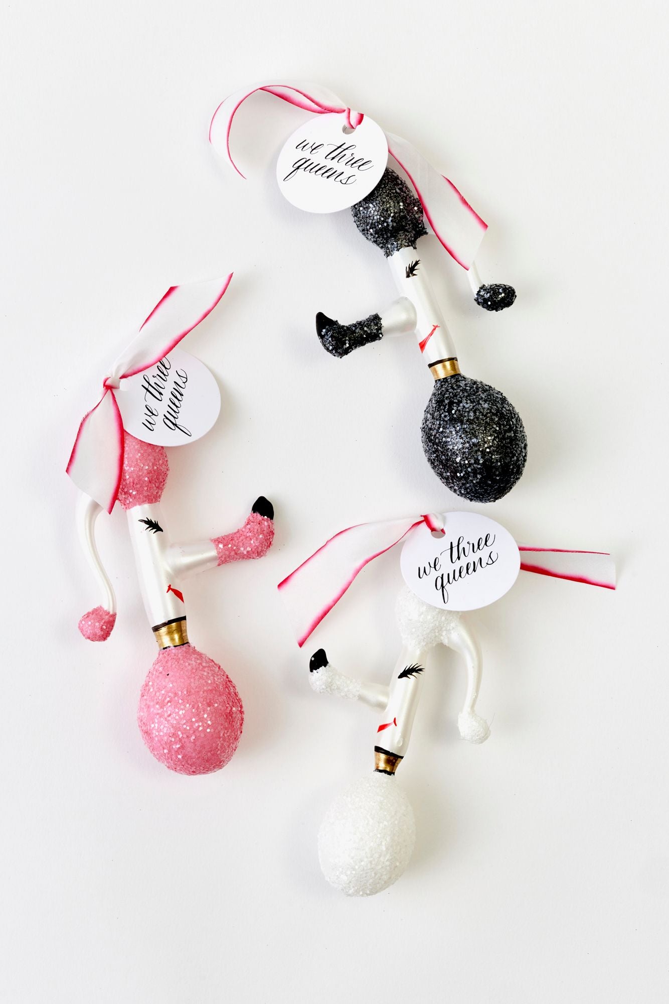 Decorative poodle ornaments with 'we three queens' tags on a white background