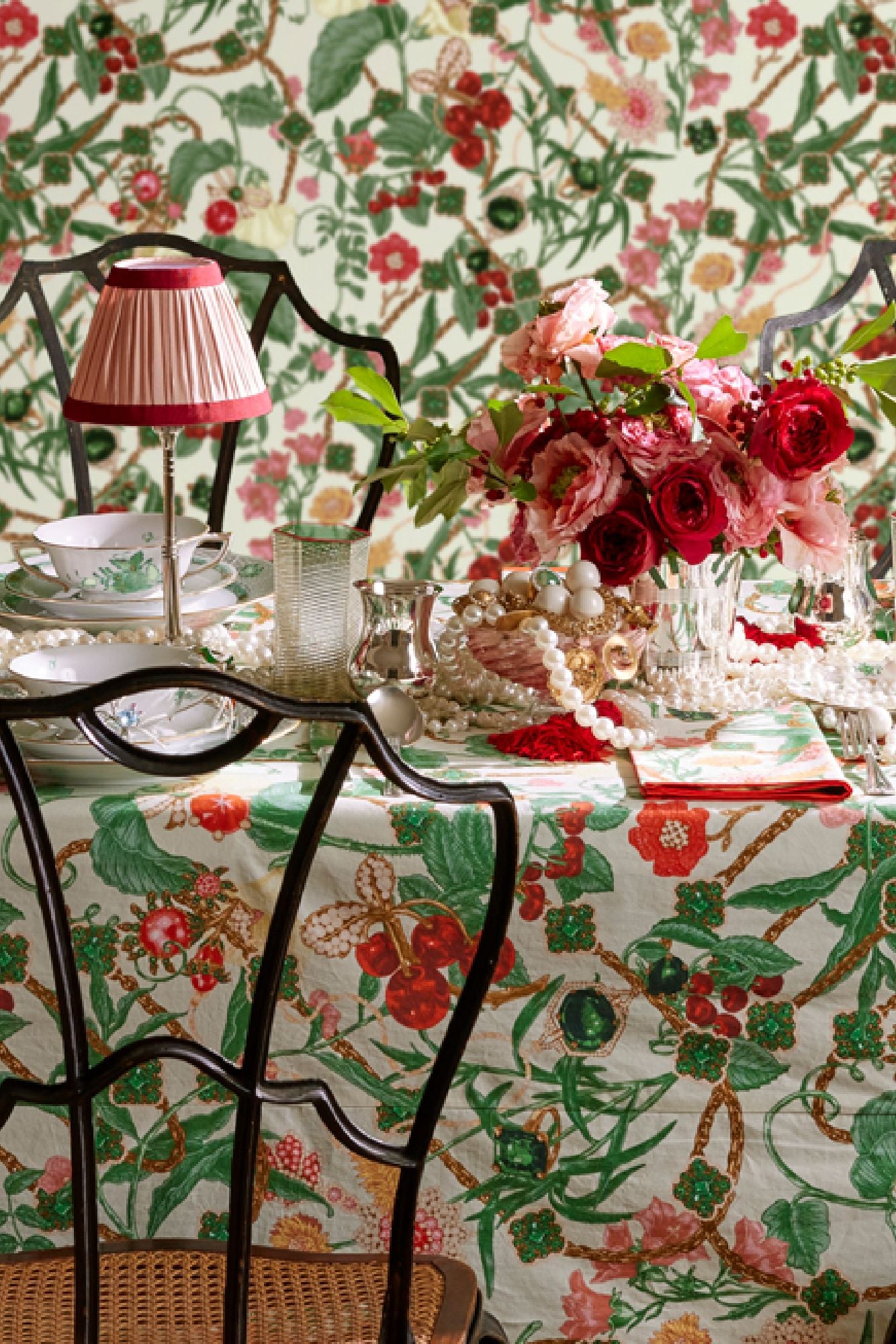 Table setting with floral tablecloth, chairs, and flowers against a floral wallpaper background