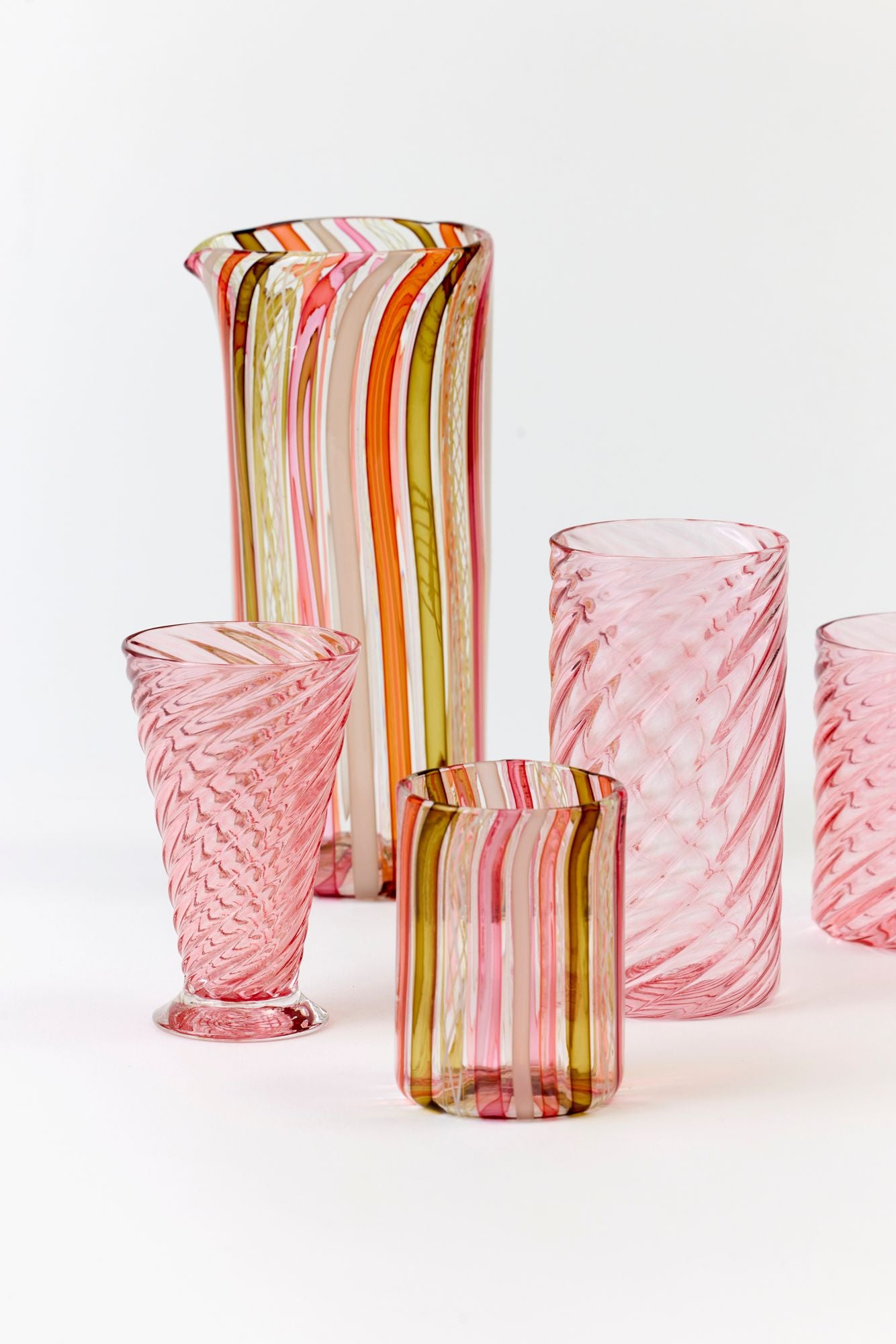 Set of colorful glasses and pitcher on a white background