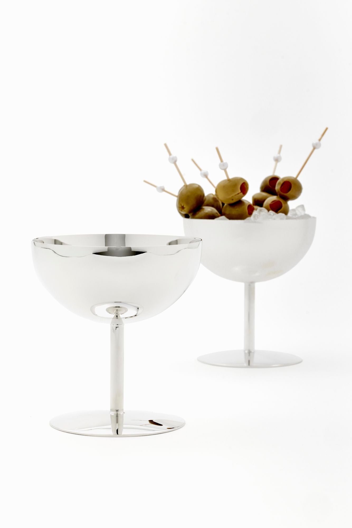 Two silver cocktail glasses with olive skewers on a white background