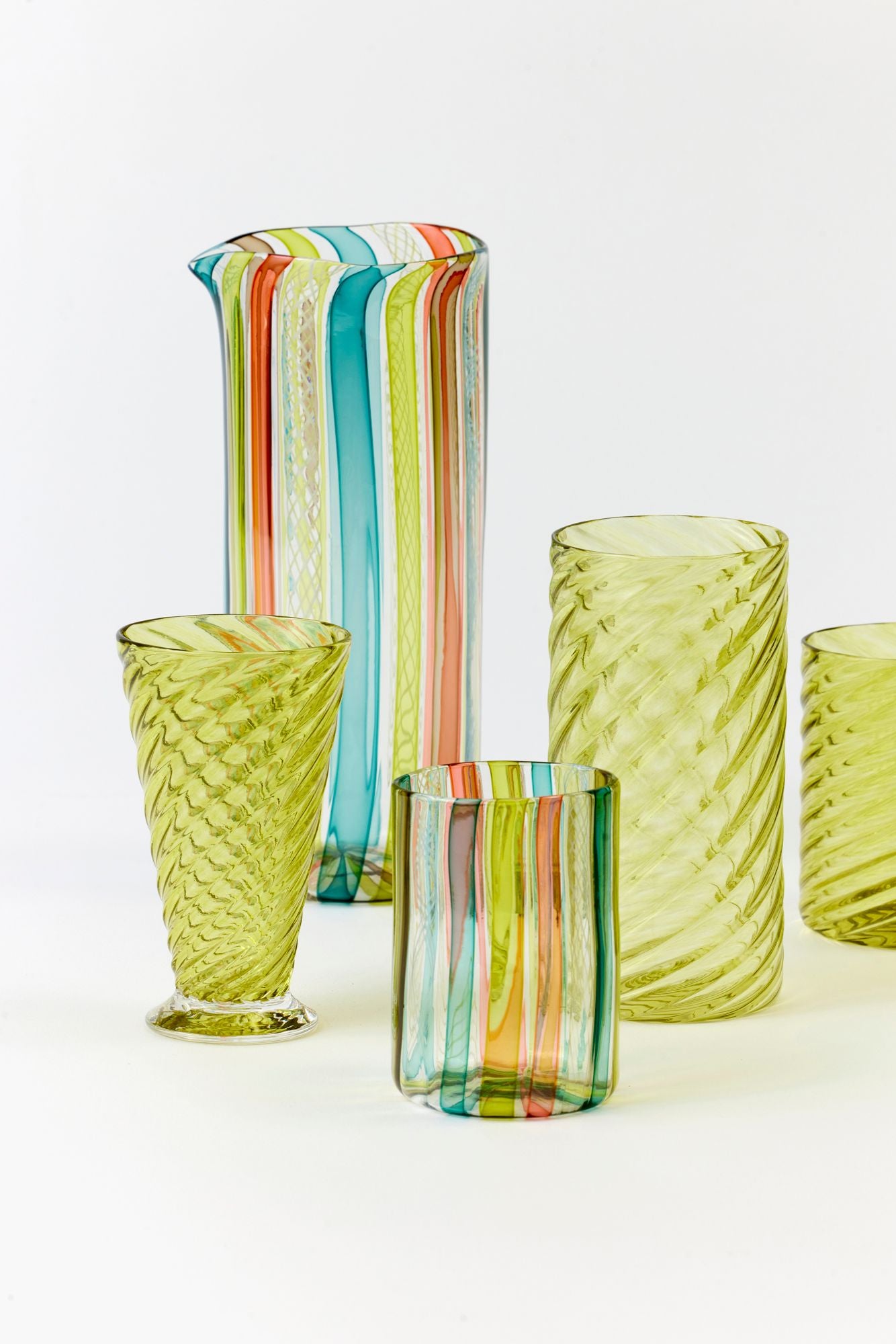 Set of colorful glass tumblers and a pitcher on a white background