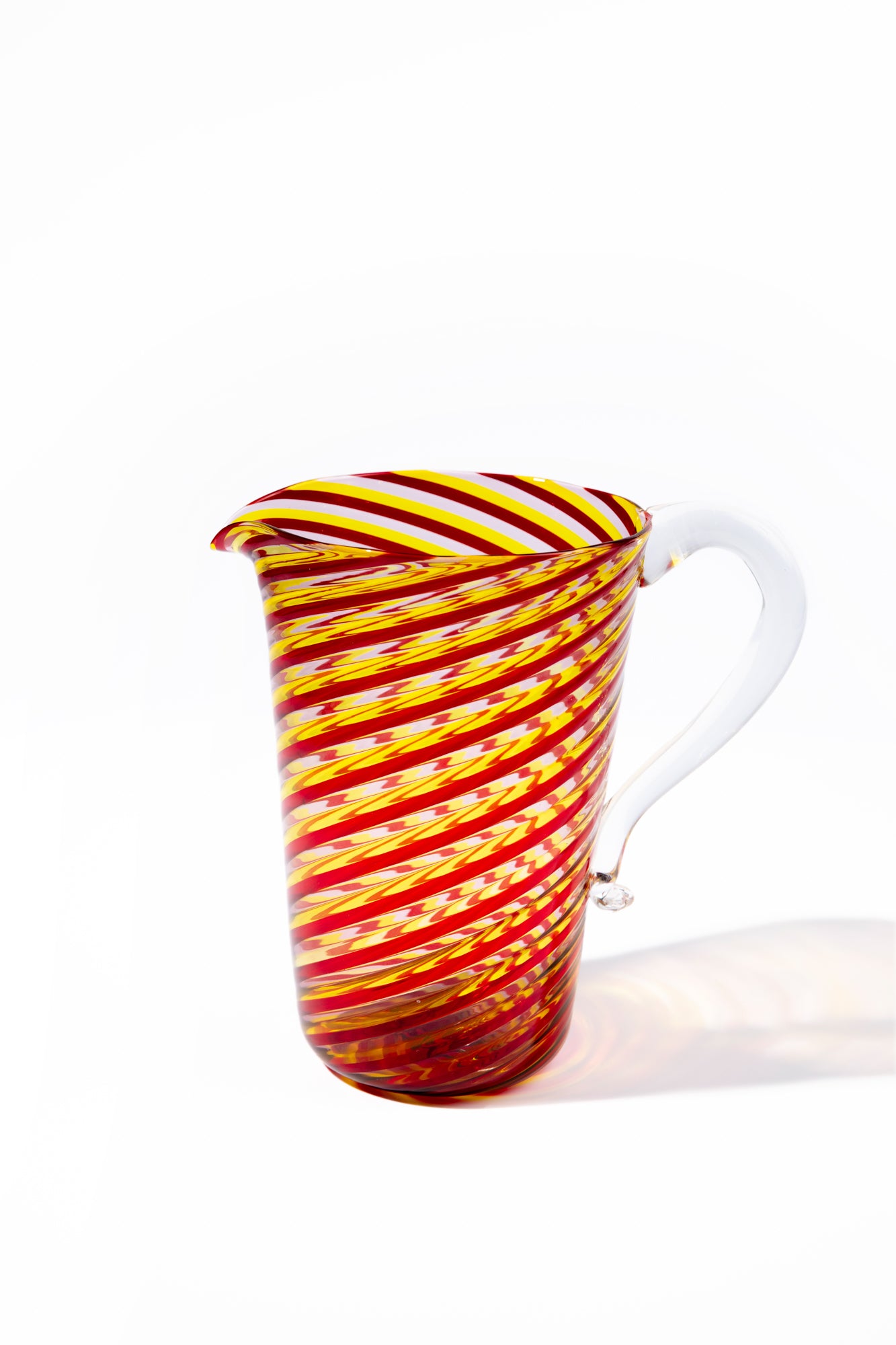 Murano twisted glass pitcher with colorful stripes of pink, red, and yellow and a clear glass handle. 