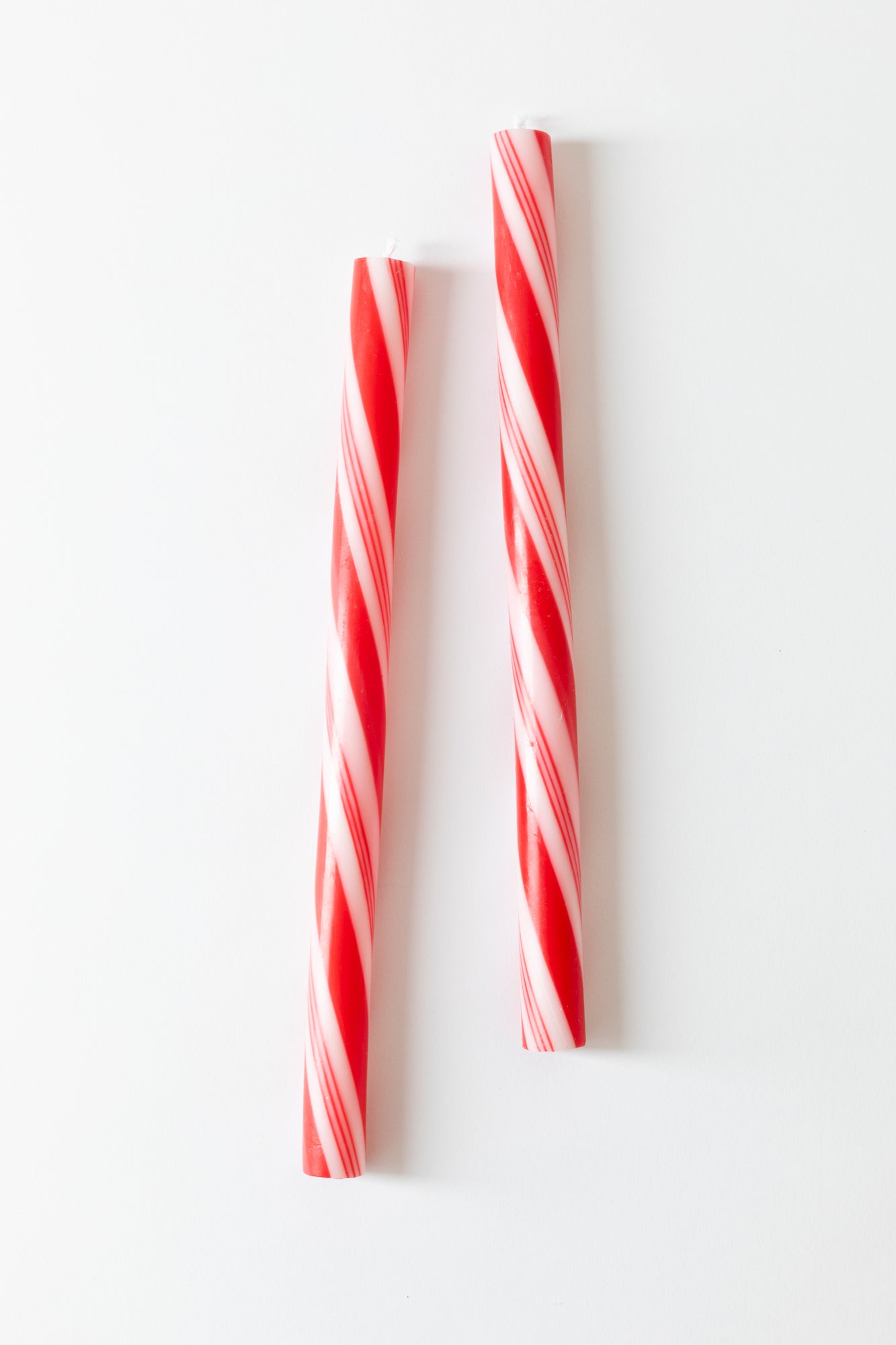 Photograph of two 12 inch taper candles with a red and white peppermint twist design. 