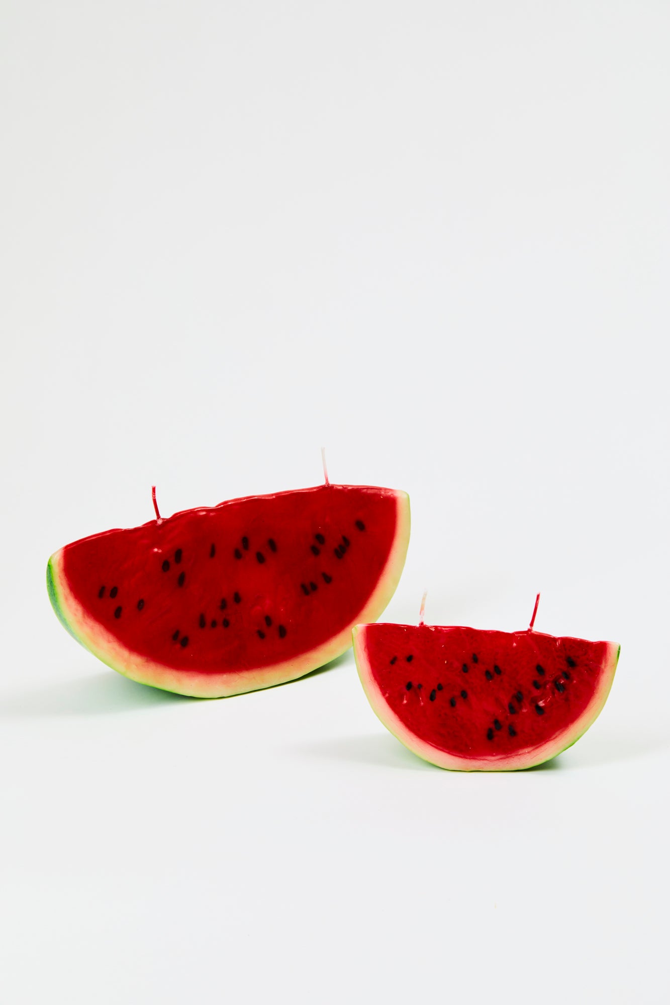 Two candles designed to resemble a slice of watermelon, each with two candle wicks. One is larger than the other, and they are displayed on a white background. 