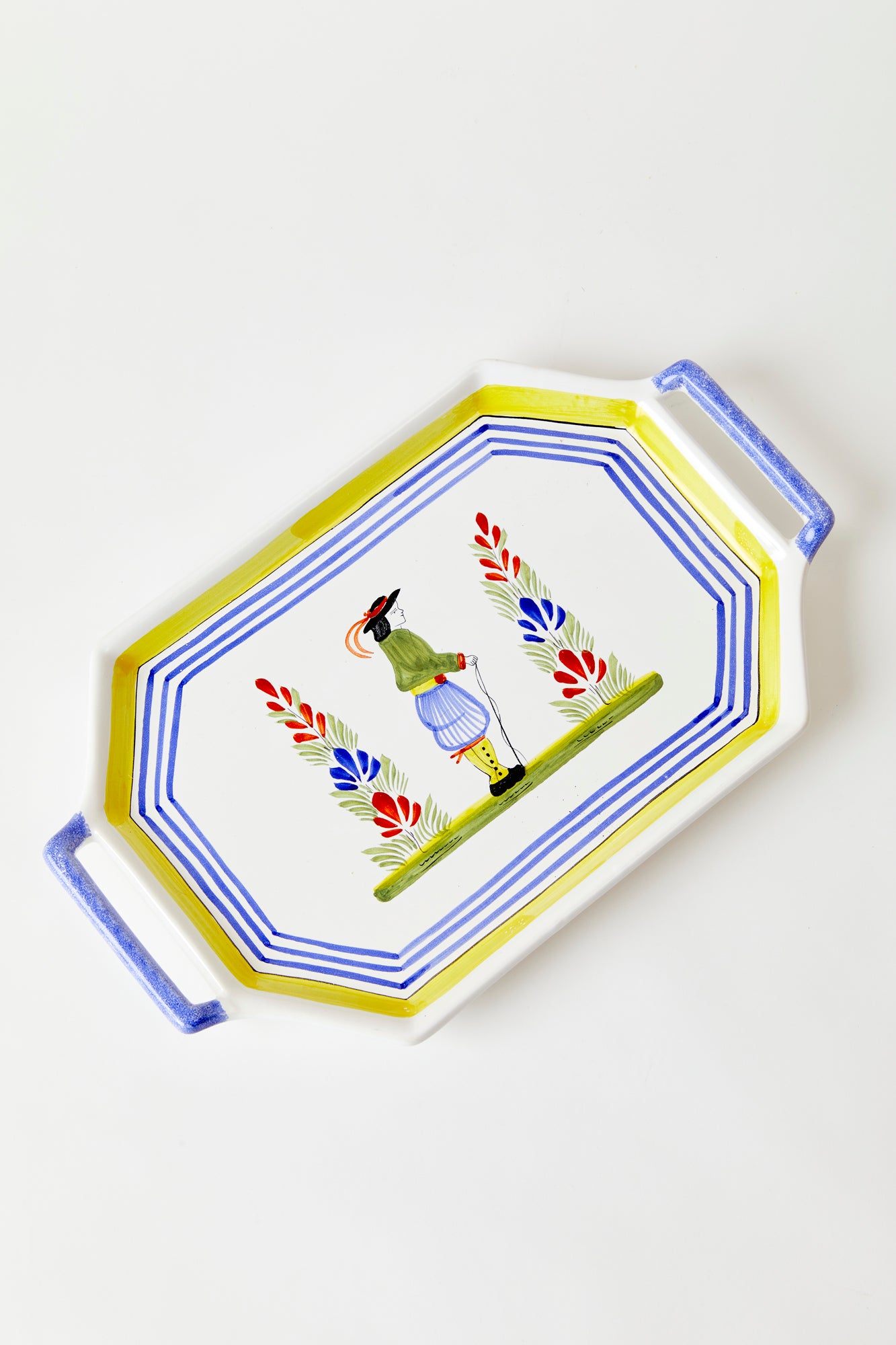 Ceramic passing tray on white background. Tray is octagonal with two blue handles. Center of tray features Dutch-inspired illustration of gentleman and two trees, surrounded by yellow and blue border.