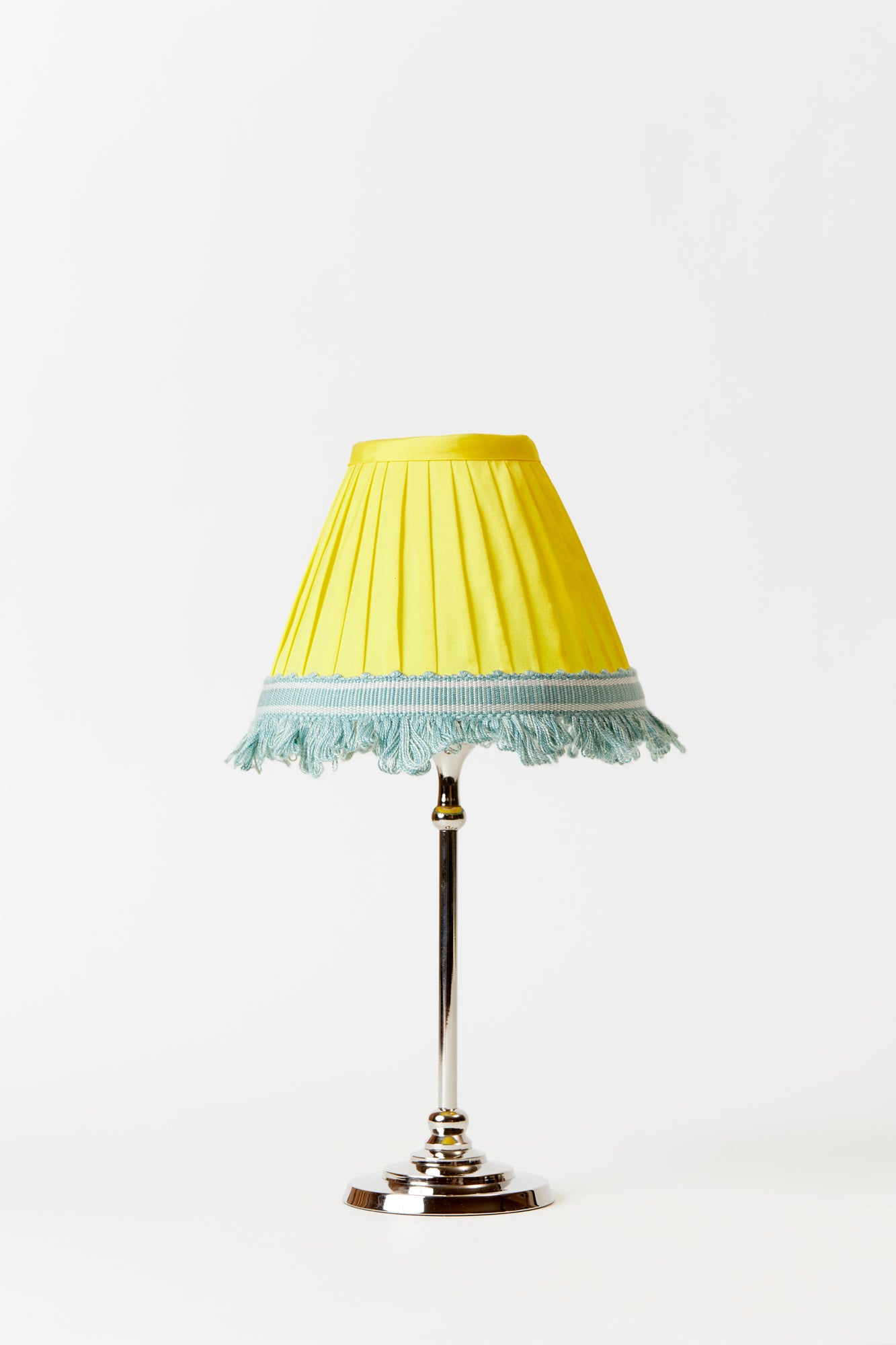 Table lamp against a white background. Base is a polished silver couple and features a yellow silk pleated lampshade with a light blue and white trim on the bottom rim. 