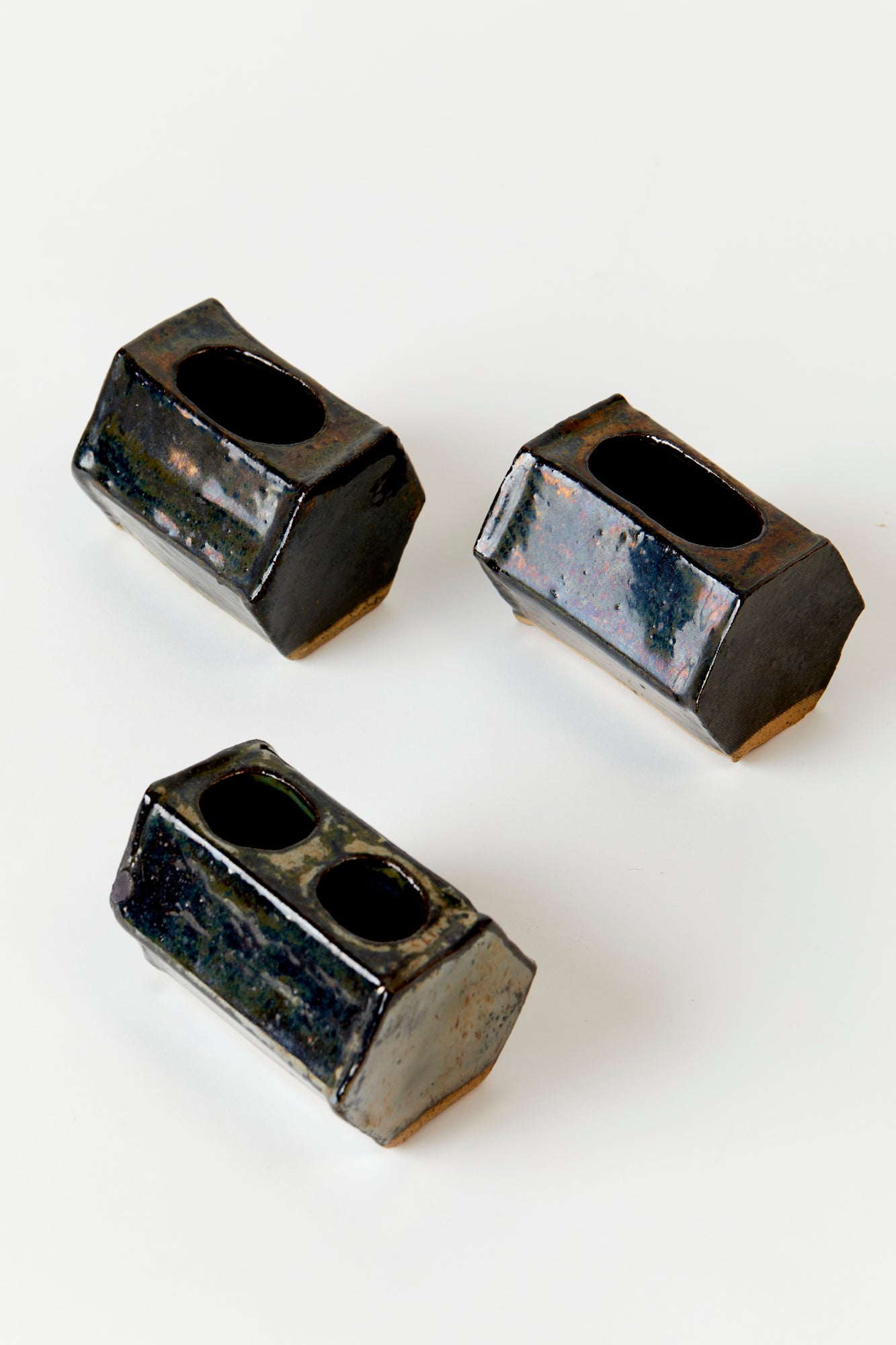 3 vintage ceramic vases on a white background. Vases are handbuilt ceramic with a dark glaze. Handbuilt in a hexagonal tube shape with different size and shape holes on top. 