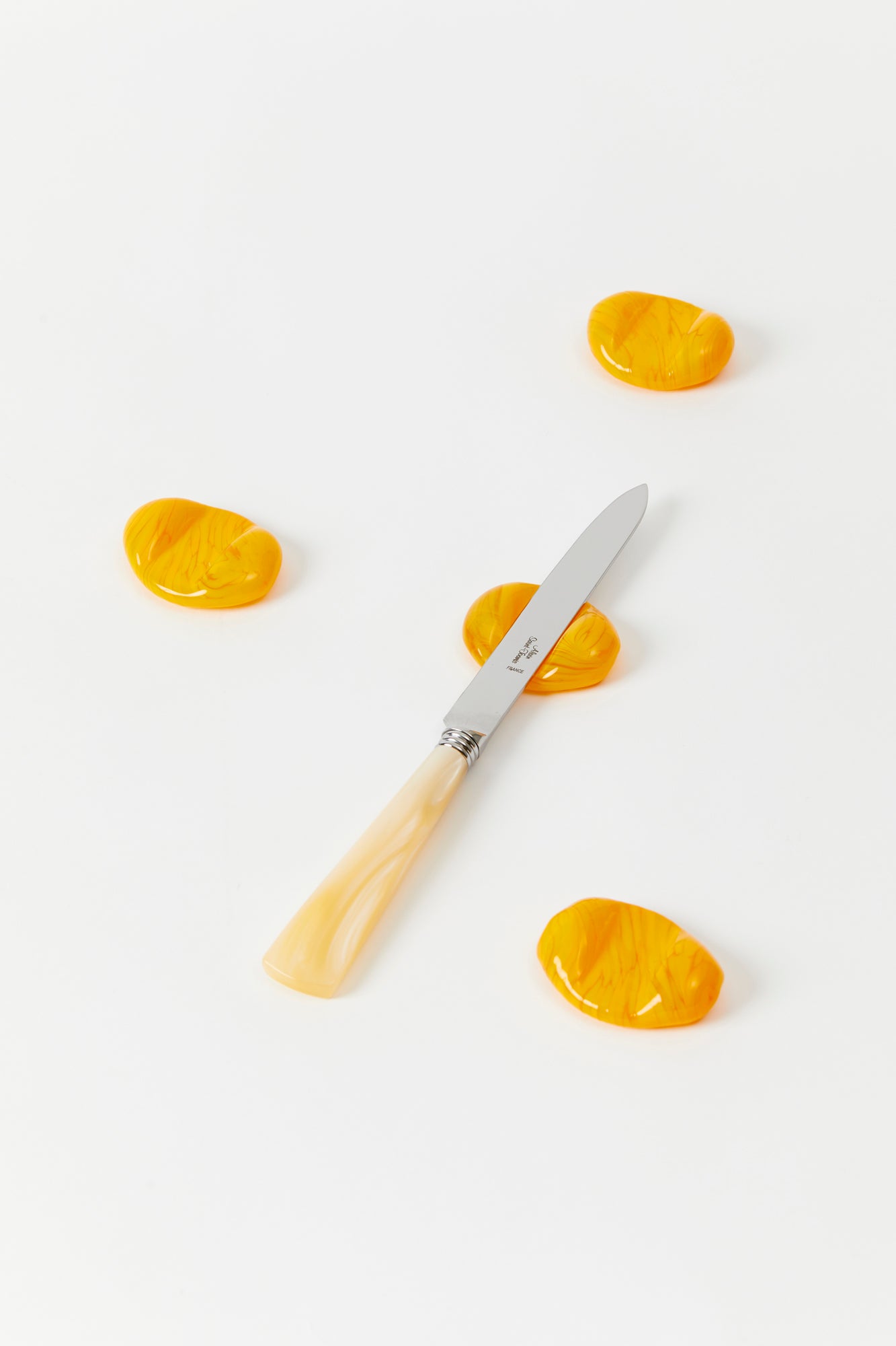 4 yellow hand blown glass knife rests on a white background, 1 with a mother of pearl knife atop. 