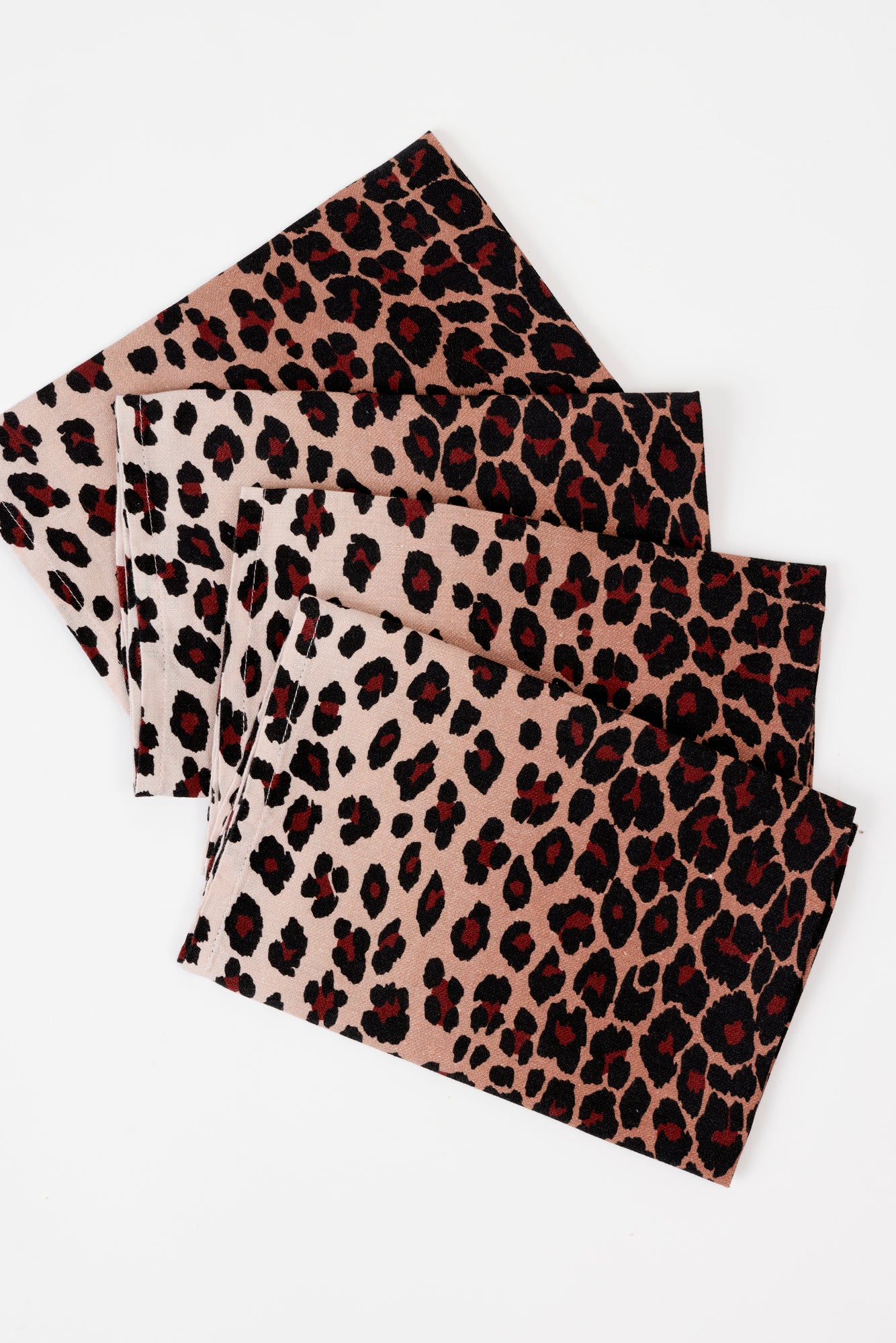 4 fabric napkins laying on a white background. Napkins are a bold cheetah print with maroon spots and light tan background. 