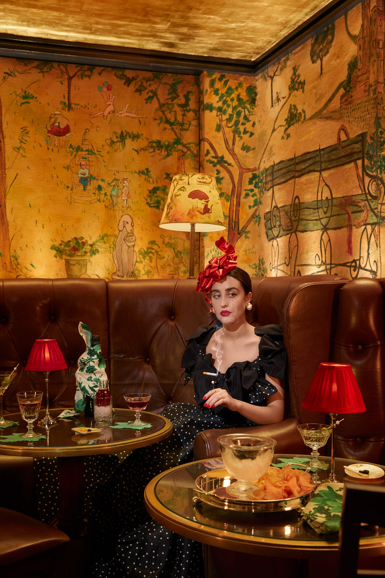 Photograph of young woman sitting in a booth in a restaurant. Table settings feature mother of pearl plates and spoons. 